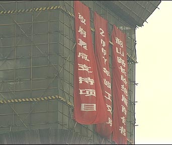 (烂尾楼外墙上挂满了大红色条幅,上面写着:政府重点支持项目,2007年