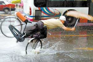 记者抓拍骑车人暴风雨中遇水坑摔倒遭网民痛骂