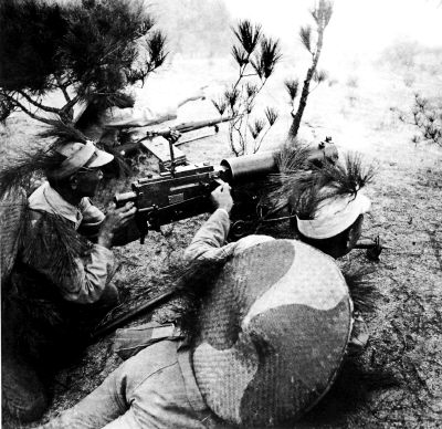 在抗日军队重机枪阵地,军帽上别着伪装用的树枝的射手们正在操纵重