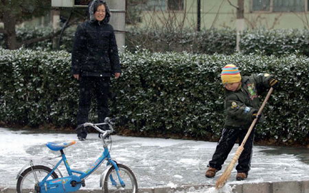 图文:小朋友在妈妈的陪伴下打扫路边的积雪