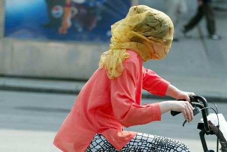 5月15日,一女青年用纱巾蒙头,以抵挡烈日和大风