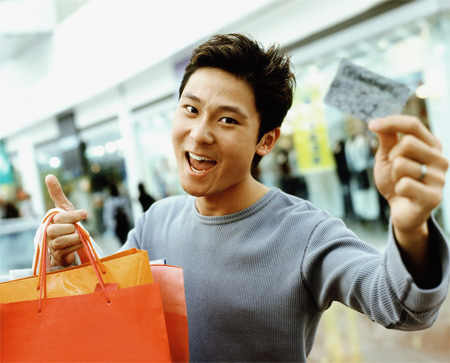 图文:年轻男人笑着手持购物袋和信用卡