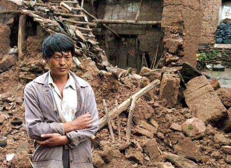8月6日,一名男子站在云南省会泽县娜姑镇地震灾区倒塌的房屋前
