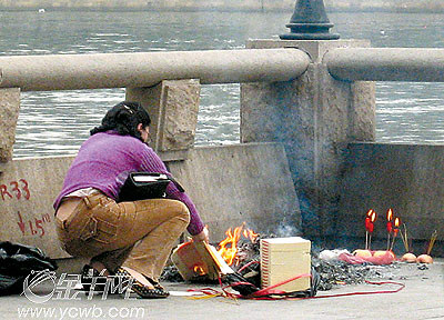 周日,爱群大厦对开的长堤边,一女士燃起香烛燃烧冥钱祭奠