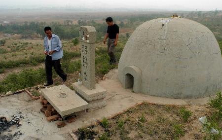 两位村民从林地里一座水泥结构的墓穴前走过